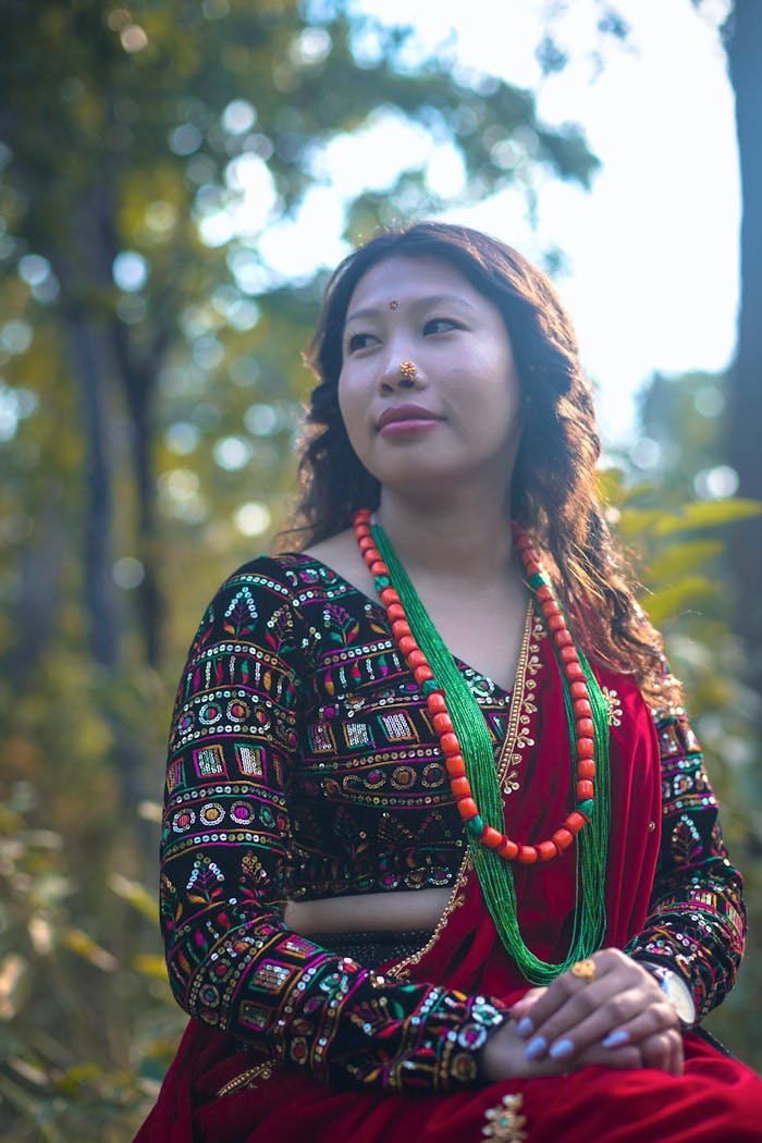 A Magar woman in traditional clothing and jewelry in an outdoor Nepalese setting.